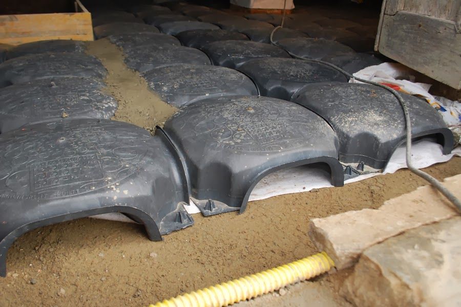 File di tegole nere impilate a terra in un cantiere sotto una struttura