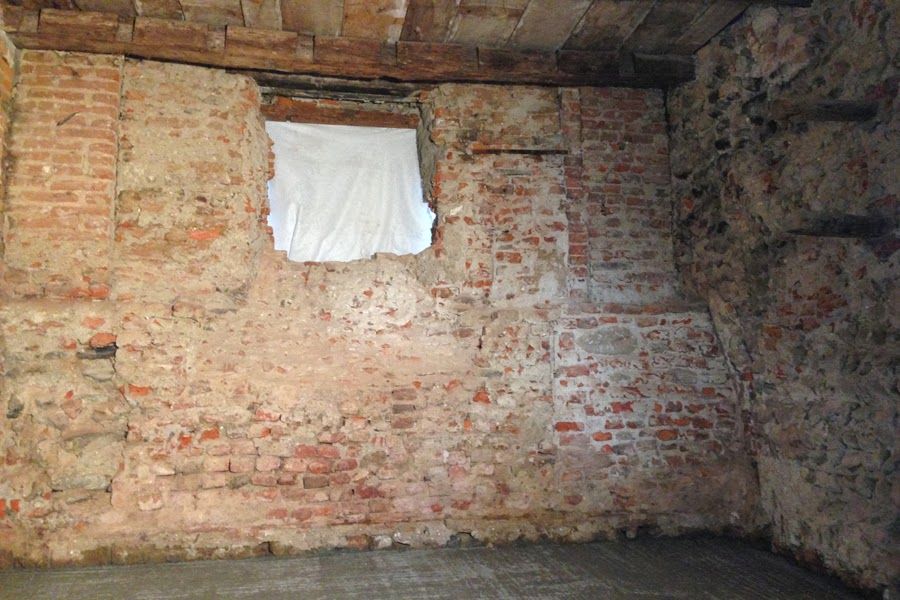 Parete del seminterrato in mattoni a vista con una piccola finestra coperta da un panno bianco vicino al soffitto.