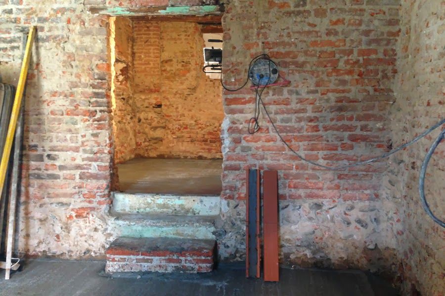 Porta in mattoni in una parete interna grezza con gradini consumati e fili elettrici a vista.