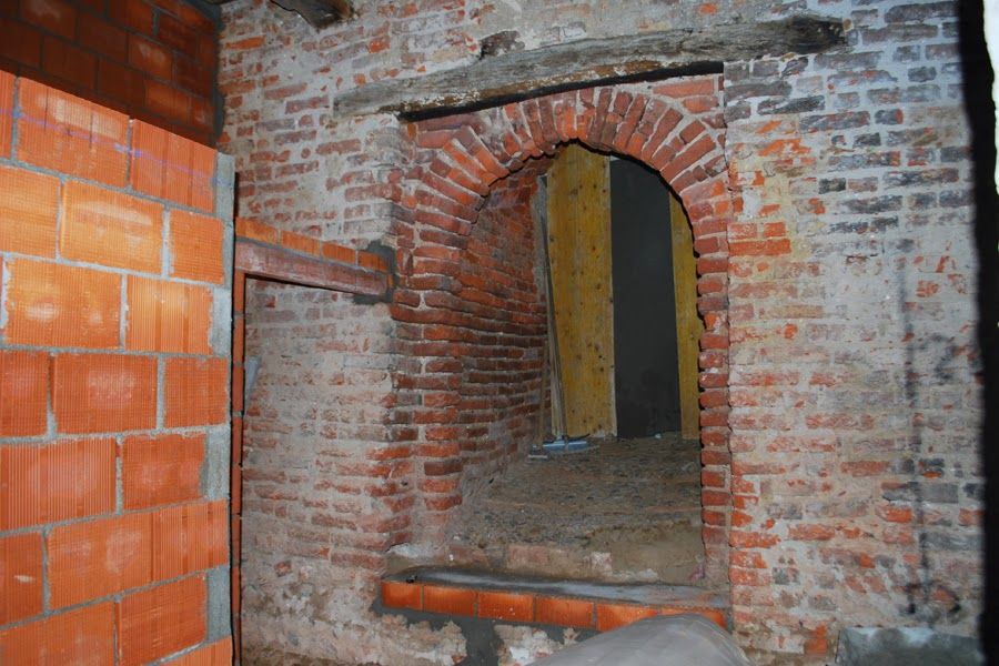 Apertura ad arco in mattoni in una parete interna non rifinita con mattoni a vista e una stretta porta oltre