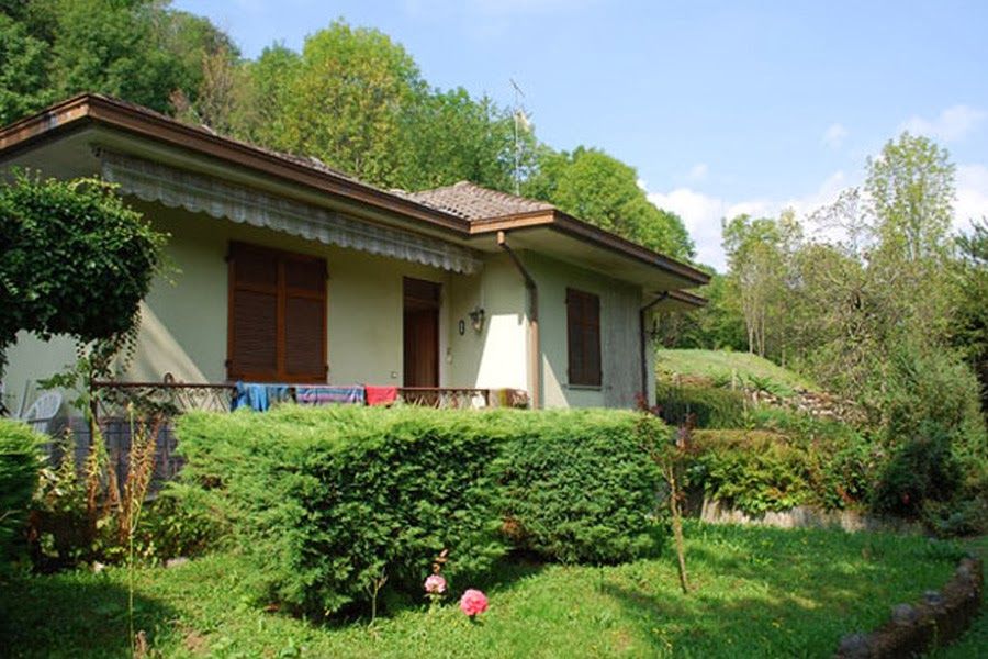 Piccola casa con persiane marroni circondata da un rigoglioso giardino verde e alberi in una giornata di sole
