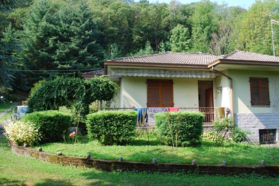 Piccola casa con tetto di tegole, persiane in legno e giardino circondato da alberi.