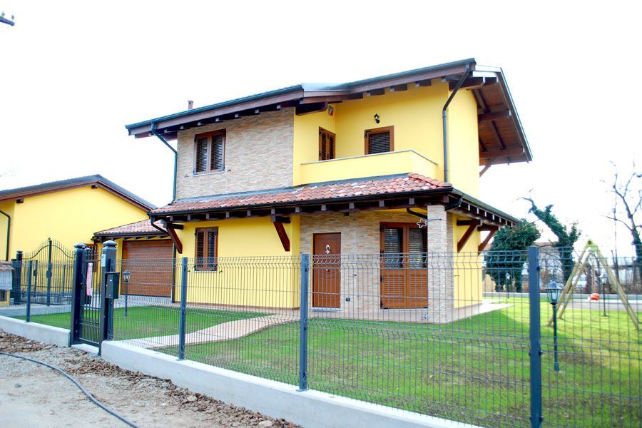 Casa gialla a due piani con cortile recintato e vialetto d'accesso sotto un cielo nuvoloso