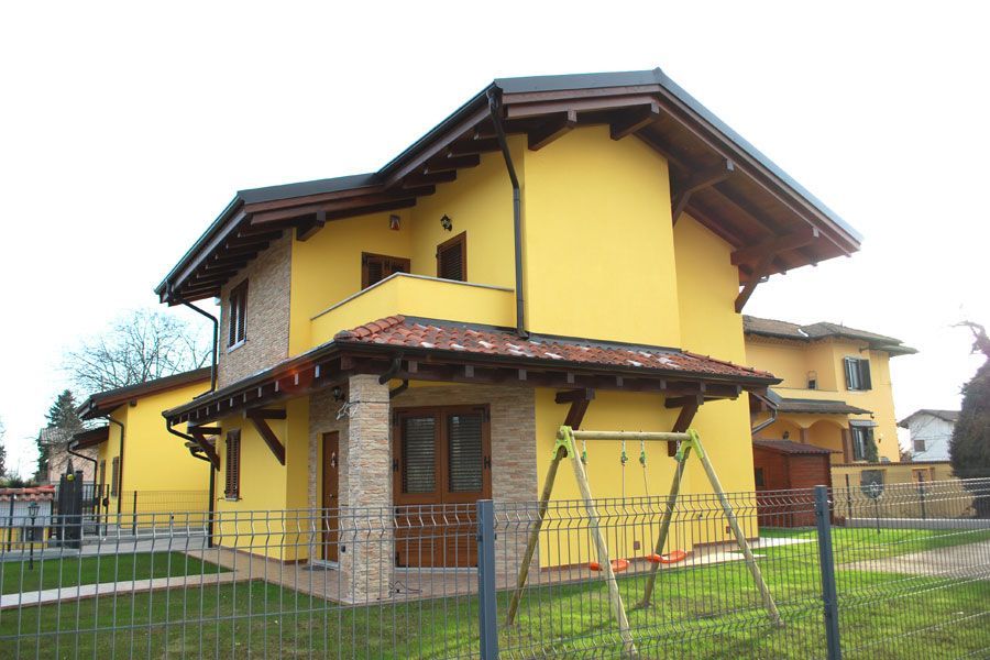 Casa gialla a due piani con tetto marrone e cortile recintato in una giornata nuvolosa.