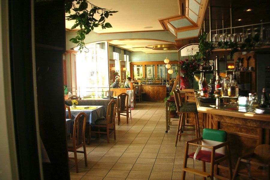 Accogliente interno di un ristorante con tavoli in legno, pavimento piastrellato e calda luce solare proveniente da sinistra.