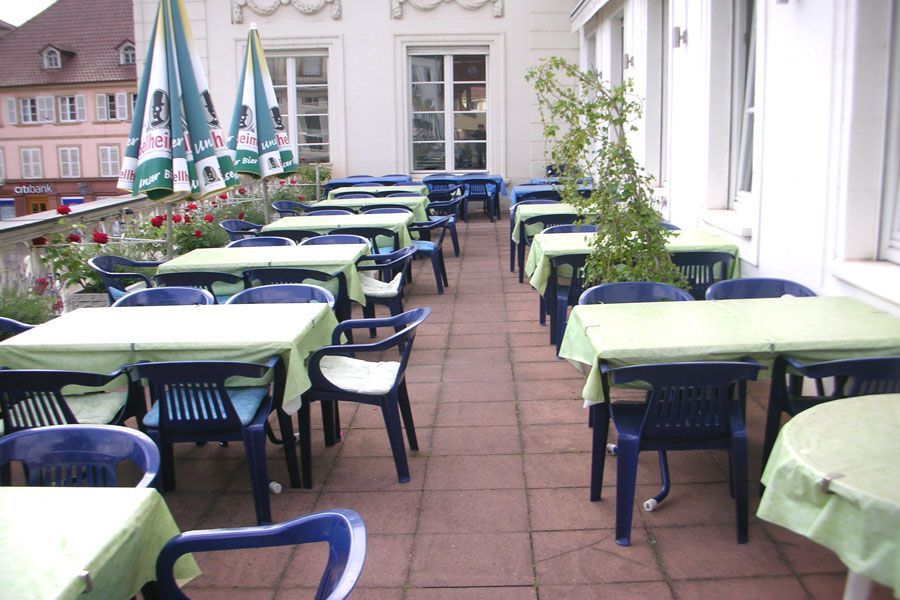 Tavolini all'aperto con tavolini verdi e sedie scure lungo la terrazza dell'edificio.