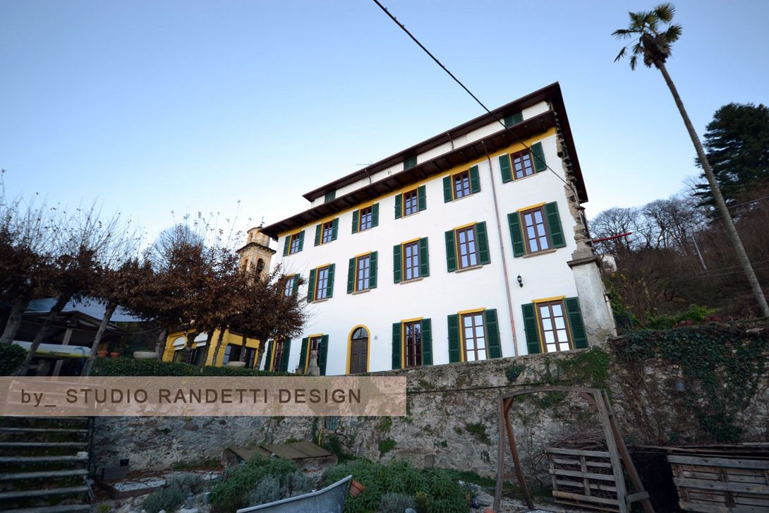 Edificio bianco con persiane verdi su una collina, visto dal basso contro un cielo azzurro.