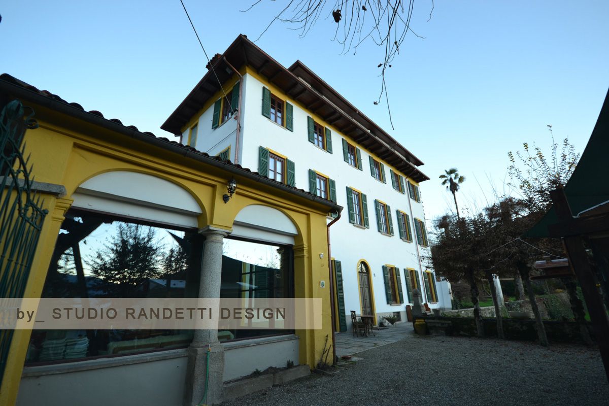 Villa gialla e bianca con cancello ad arco e cortile sotto un cielo azzurro