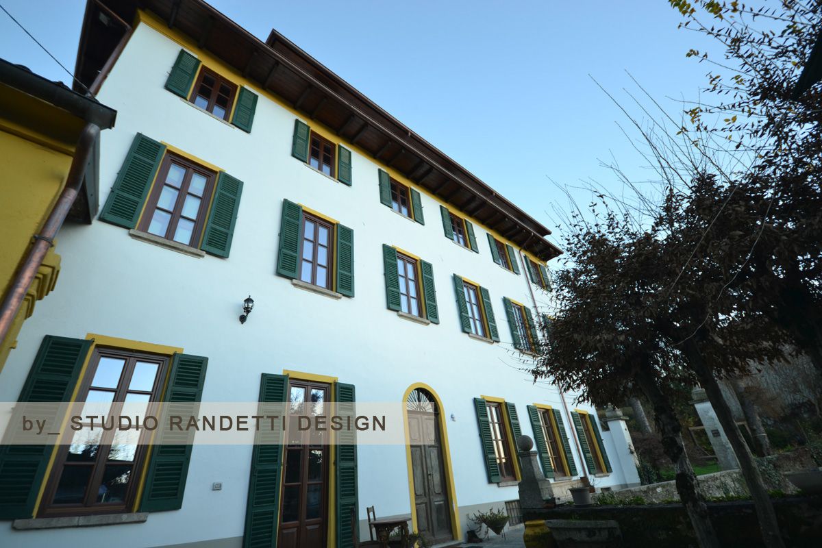 Edificio bianco con persiane verdi e porta gialla accanto ad alberi sotto un cielo azzurro limpido.