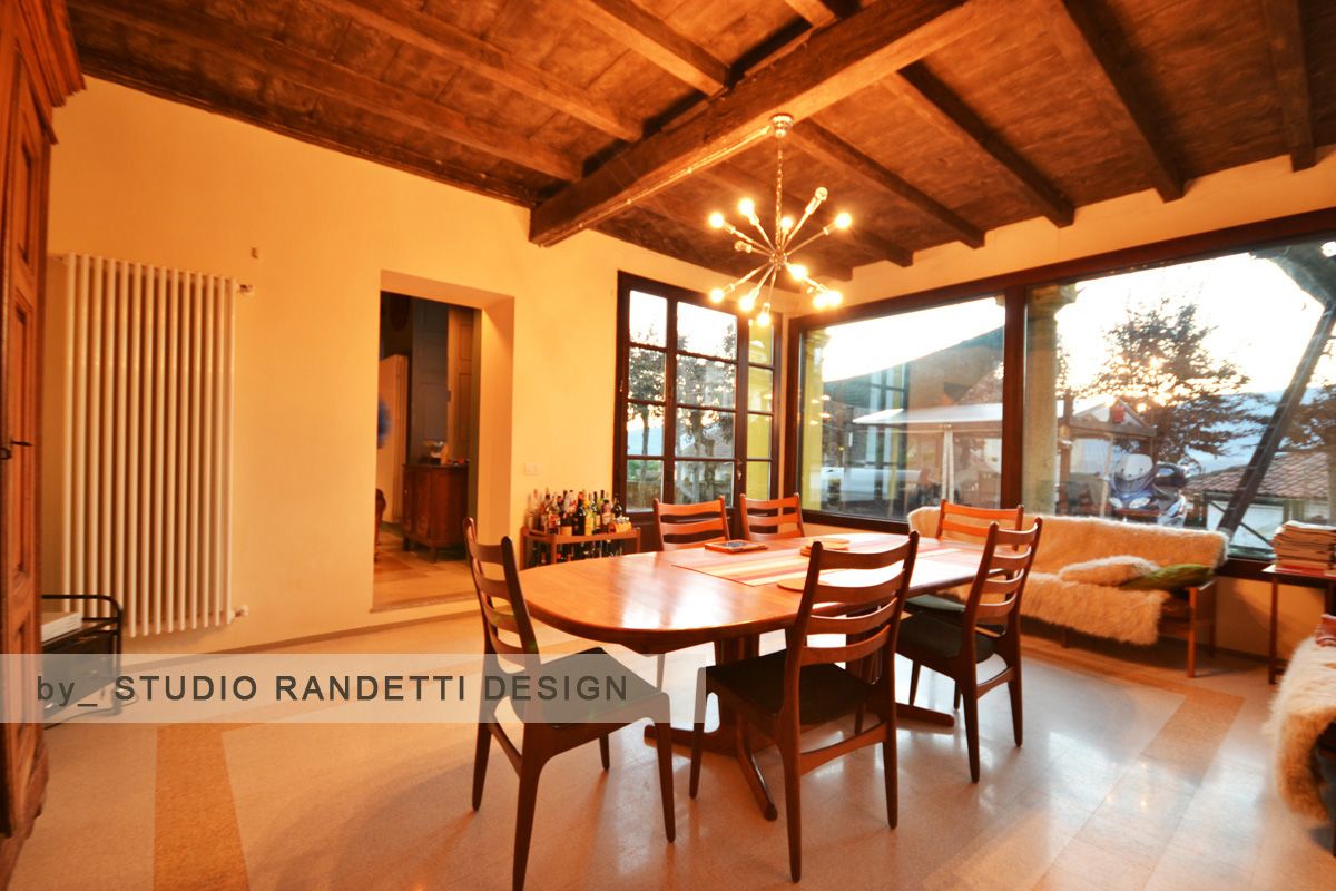 Accogliente sala da pranzo con tavolo e sedie in legno, soffitto a volta e grandi finestre al tramonto.
