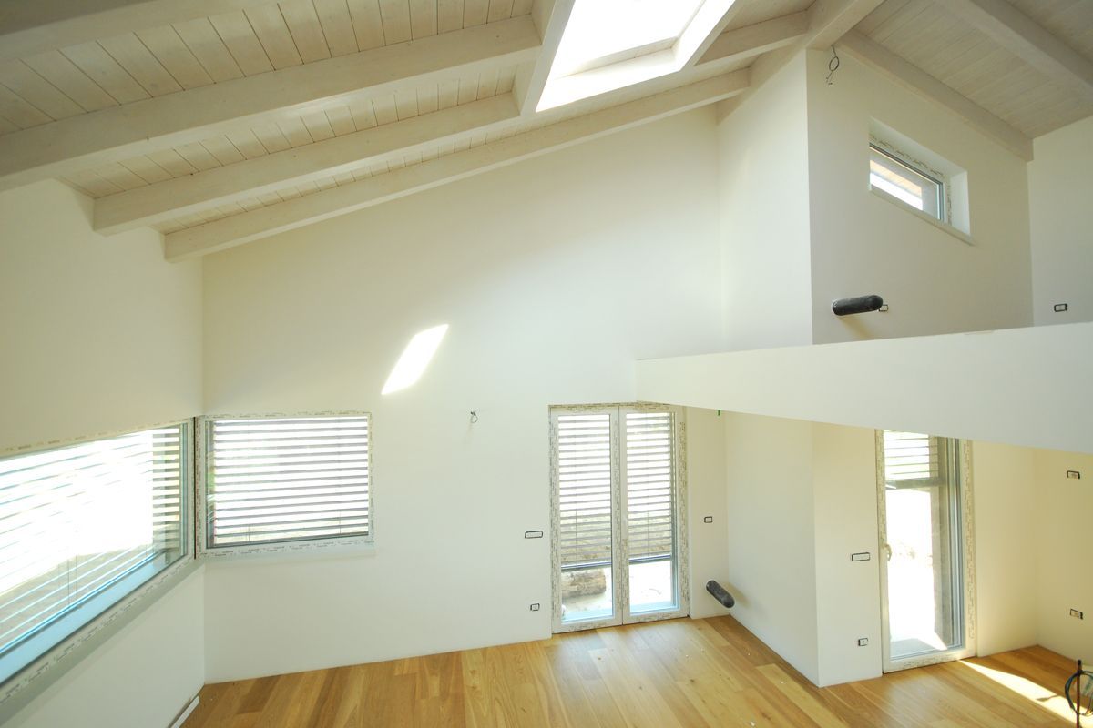 Luminosa mansarda vuota con pavimento in legno, soffitto alto, lucernari e persiane bianche.