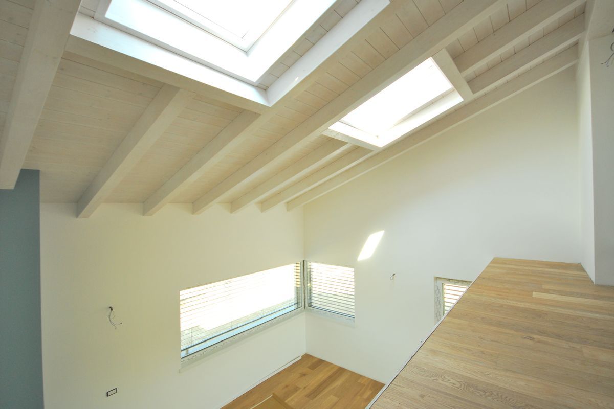 Luminoso loft vuoto con pareti bianche, lucernari, pavimento in legno e ringhiera che si affaccia su un livello inferiore.