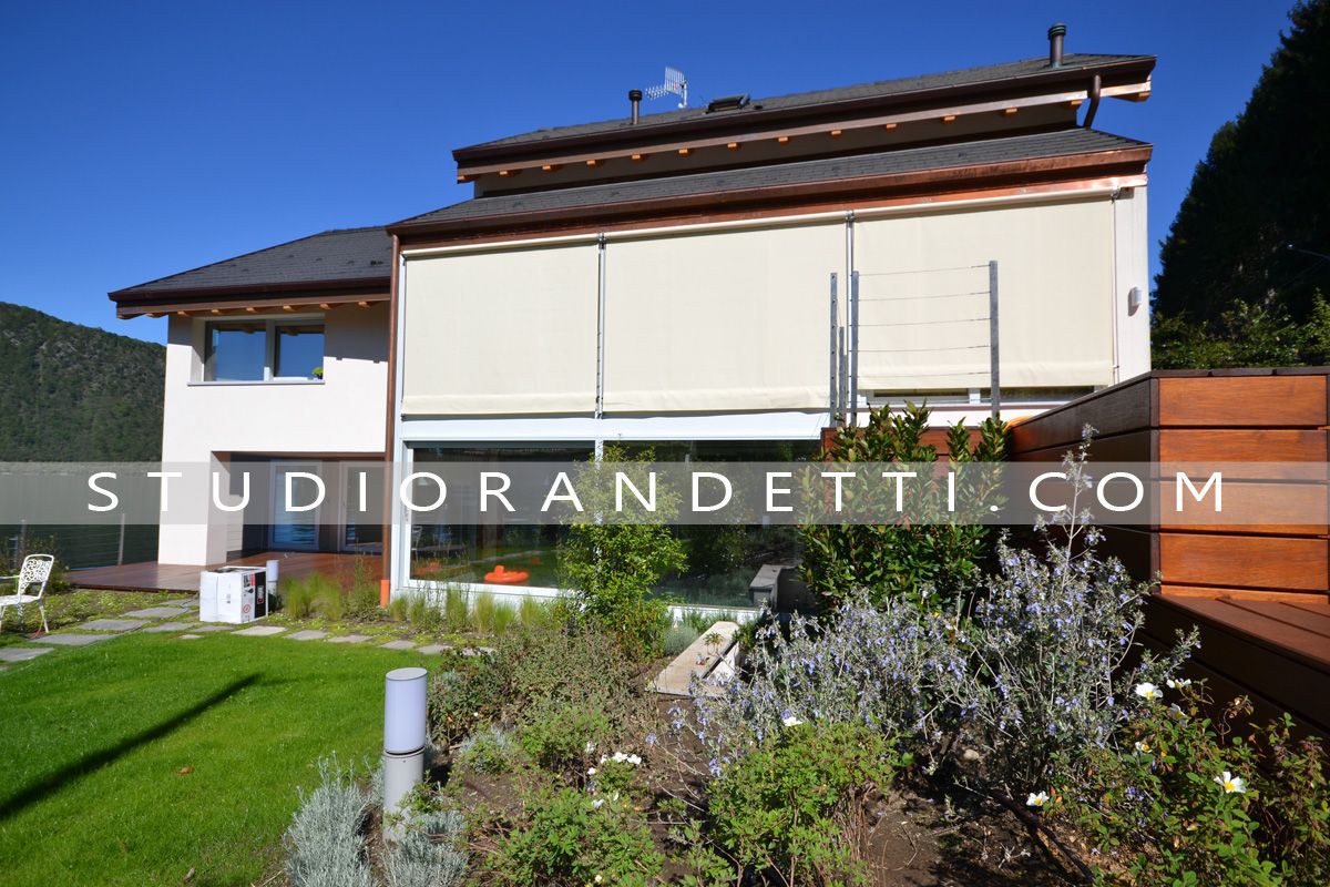 Casa moderna bianca con tetto marrone accanto a un giardino in piena luce solare, con una filigrana al centro.