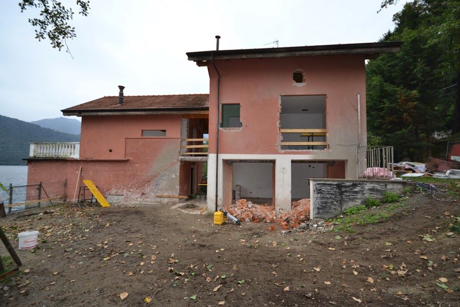 Casa rosa parzialmente costruita, con mattoni a vista e macerie, in un cantiere fangoso.