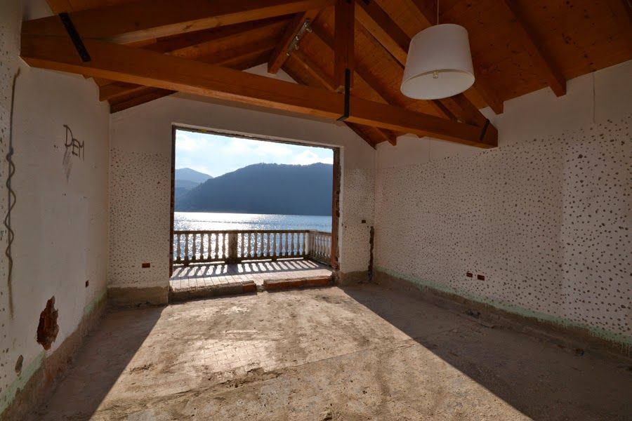 Stanza vuota con soffitto con travi in ​​legno, porta finestra aperta sul balcone e vista sul lago di montagna.