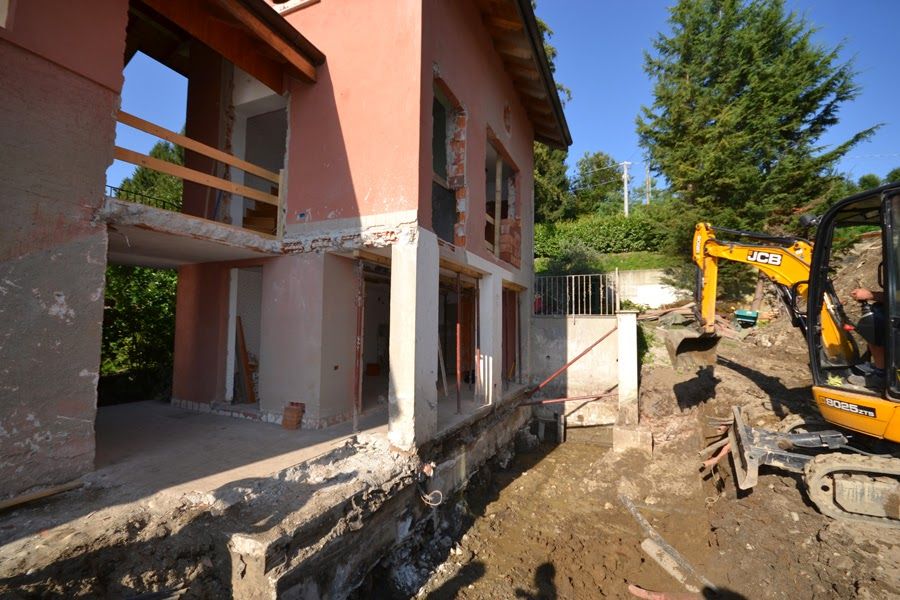 Cantiere edile accanto alla casa rosa con un escavatore che scava terra e detriti