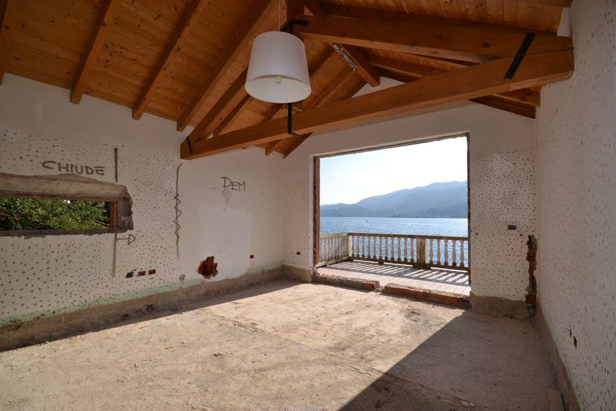 Stanza rustica vuota con soffitto in legno, vista mare attraverso la porta aperta e montagne sullo sfondo.
