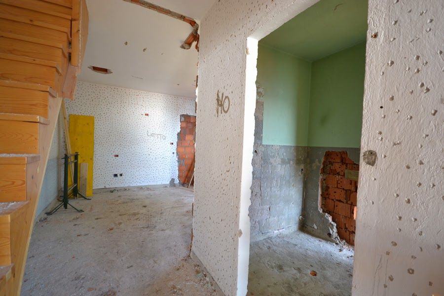 Interno parzialmente ristrutturato con pareti non rifinite, mattoni a vista e una scala sulla sinistra.