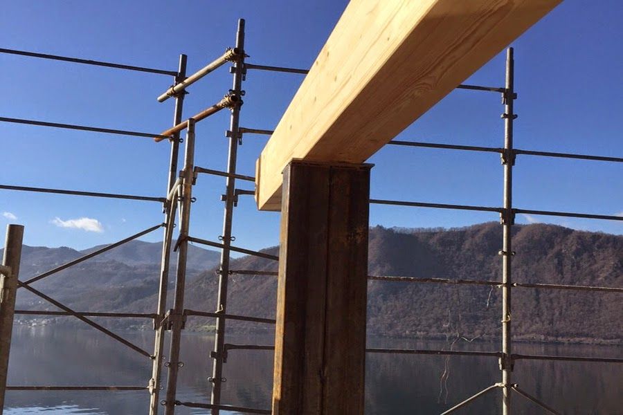 Impalcatura attorno a una trave di legno sullo sfondo di montagne sotto un cielo azzurro.