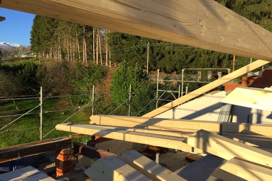 Struttura di tetto in legno parzialmente assemblata in un cantiere edile, con alberi e colline sullo sfondo.