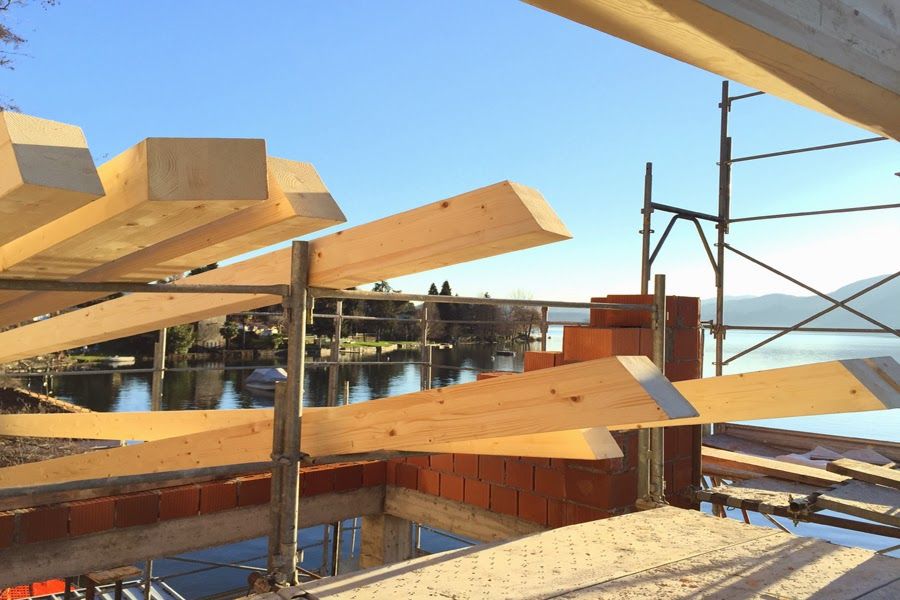 Travi di legno e impalcature in un cantiere edile affacciato sull'acqua, sotto un cielo limpido.