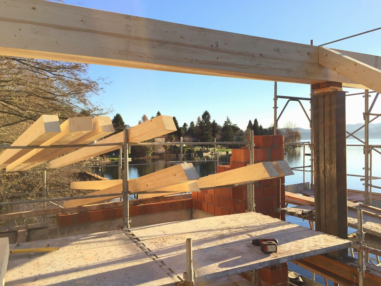 Materiali da costruzione su un balcone affacciato sull'acqua, con travi di legno e assi impilate sotto un sole splendente.