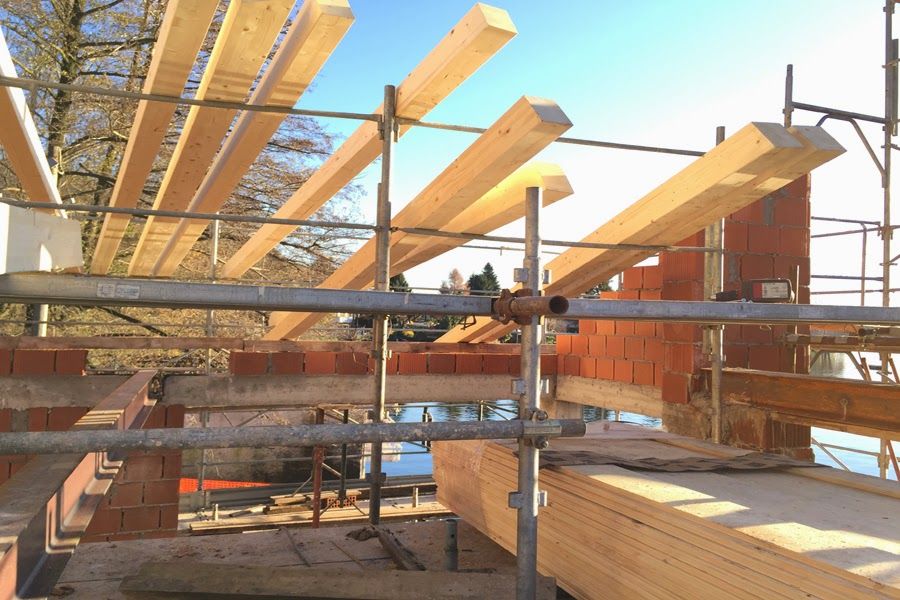 Cantiere edile con struttura in legno, impalcature e operai che costruiscono una casa sotto un cielo luminoso.