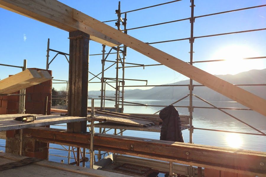 Impalcature in un cantiere edile sul lungomare all'alba, con travi e un operaio stagliati contro il sole.