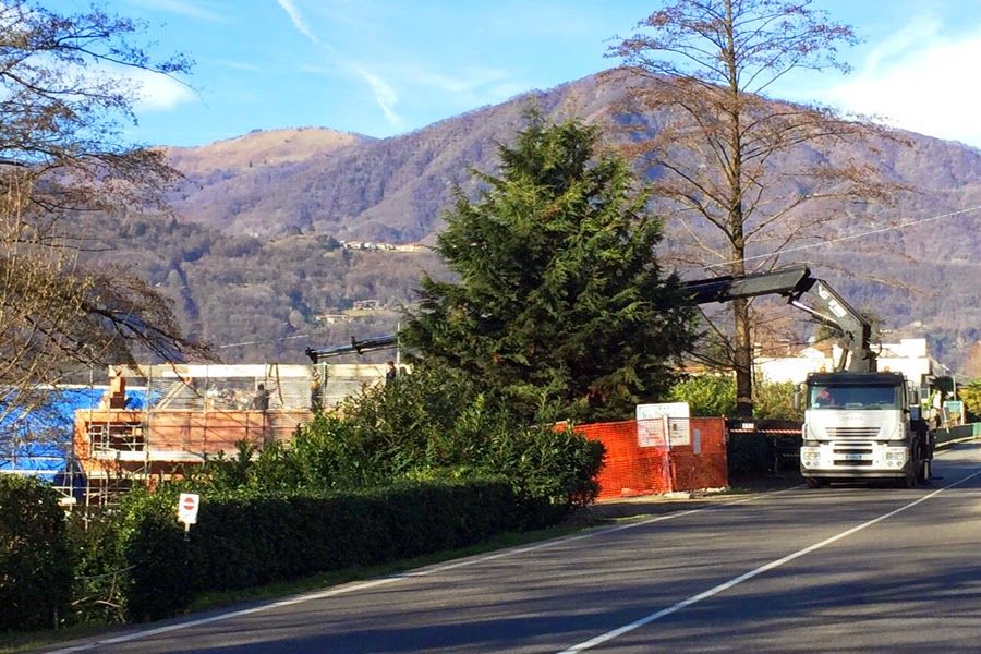 Una strada di montagna con un camion, case, alberi e un lago sotto un cielo azzurro e limpido.