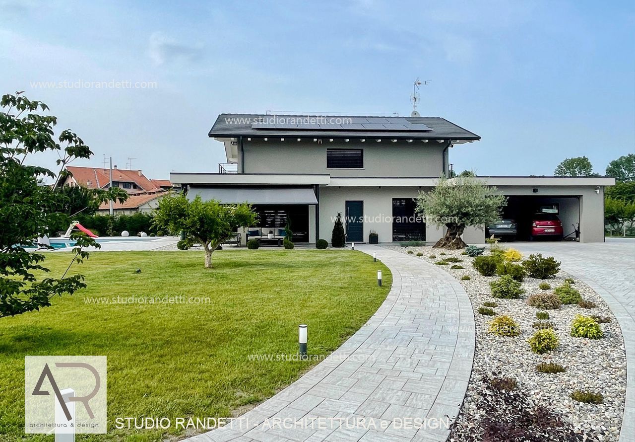 Casa moderna a due piani con vialetto d'accesso curvo in pietra, prato verde e posto auto coperto sotto un cielo limpido