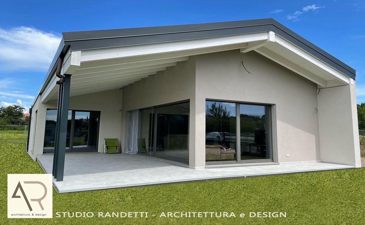 Esterno di una moderna casa bianca con ampio patio coperto, tetto spiovente e porte finestre aperte.