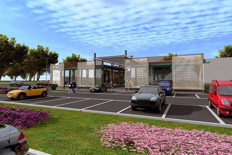 Esterno di una moderna concessionaria automobilistica con auto parcheggiate, showroom in vetro e aiuole di fiori rosa.