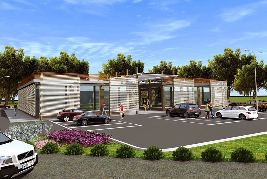 Moderno edificio per uffici in vetro con auto parcheggiate, alberi e aiuole fiorite sotto un cielo azzurro.
