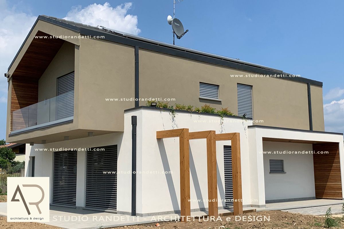 Casa moderna a due piani color beige con balcone, piano inferiore bianco e dettagli in legno sul portico sotto un cielo azzurro.