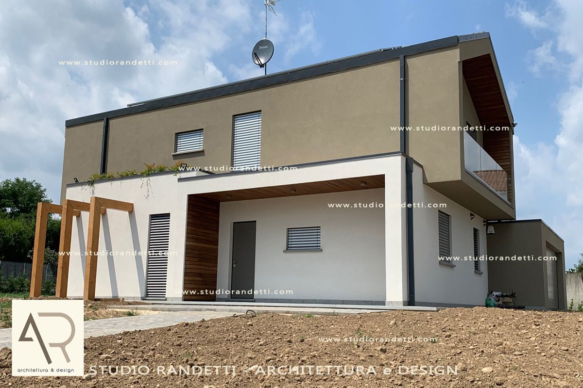 Casa moderna a due piani di colore beige con finiture bianche e pergola frontale in legno, situata su un lotto di ghiaia.