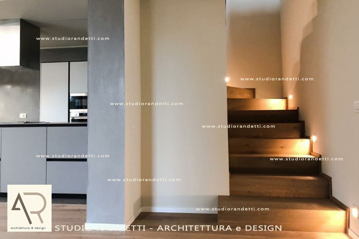 Interni moderni con scala, illuminazione calda e vista su cucina e corridoio.