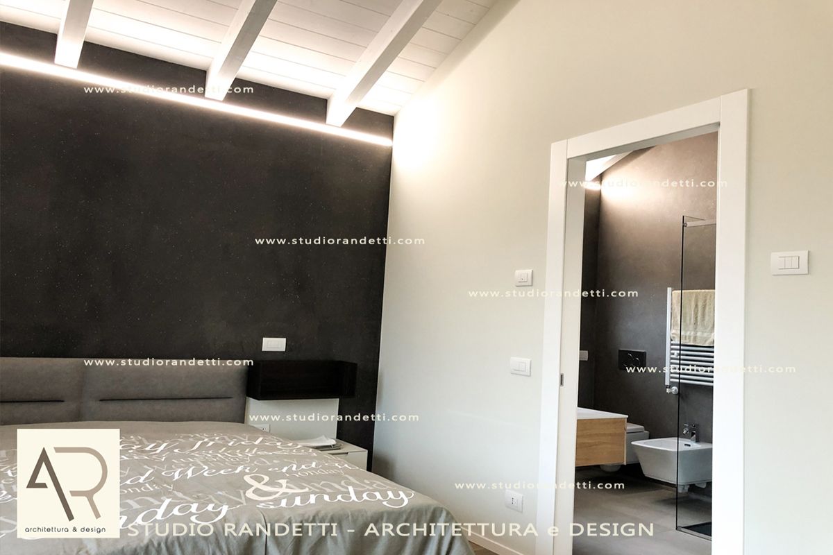 Camera da letto moderna con parete d'accento nera, letto grigio e porta del bagno aperta.