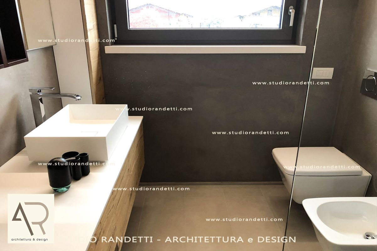 Bagno moderno con pareti nere, lavabo e WC bianchi e un'ampia finestra sopra il piano di lavoro.