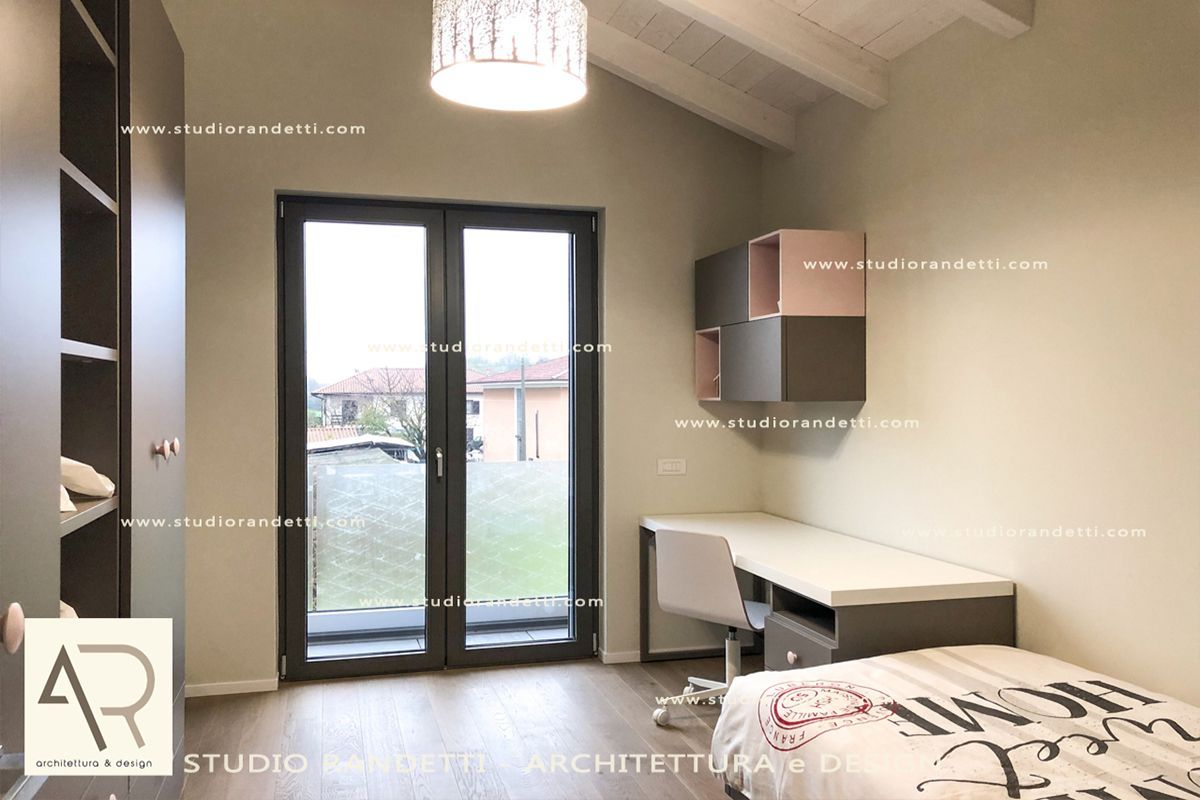 Camera da letto moderna con letto, scrivania, armadi a muro e porte finestre che si affacciano su un cortile.