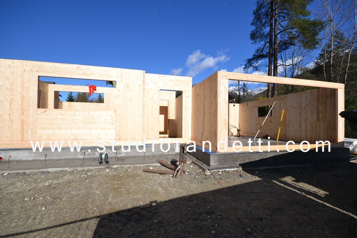 Struttura di casa in legno parzialmente costruita su un terreno ghiaioso sotto un cielo azzurro