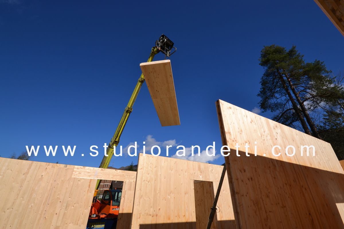Un operaio solleva un grande pannello di legno sopra una struttura in legno sotto un cielo azzurro e limpido.