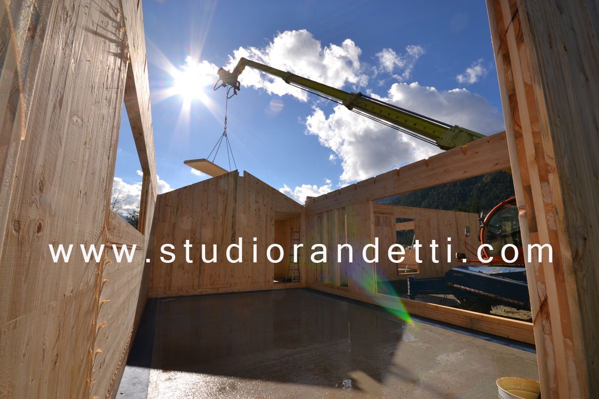 Cantiere edile con muri in cemento, braccio di gru in alto e sole splendente in un cielo azzurro.
