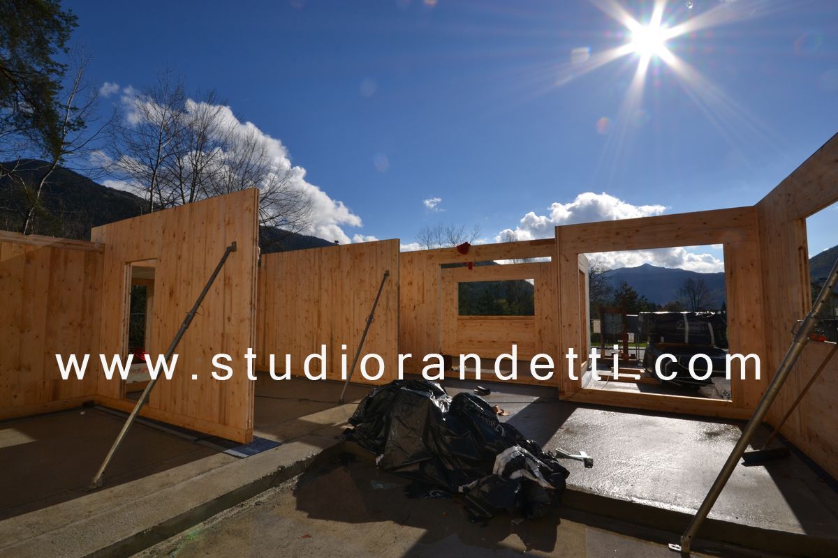 Struttura di una casa in legno parzialmente costruita, sotto un sole splendente, con le montagne sullo sfondo.