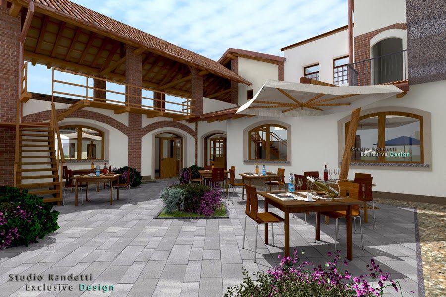 Patio del ristorante con cortile in pietra, tavoli in legno, archi, vasi di fiori e vista sulle montagne.