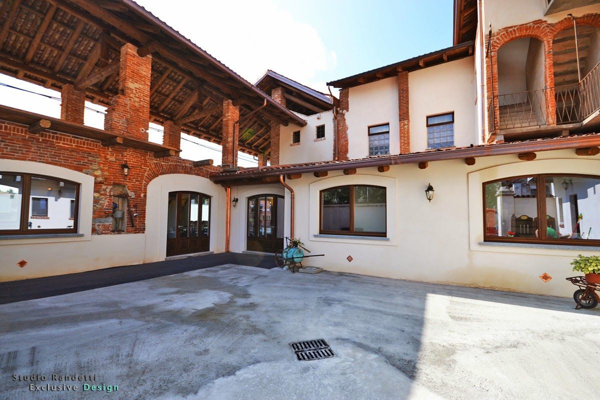 Cortile soleggiato con edifici in mattoni e stucco, portali ad arco e finestre che circondano un patio in cemento.
