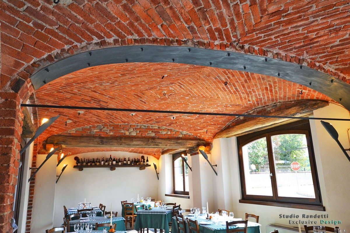 Sala da pranzo rustica con soffitto a volta in mattoni a vista, travi in legno e tavoli disposti sotto le finestre.