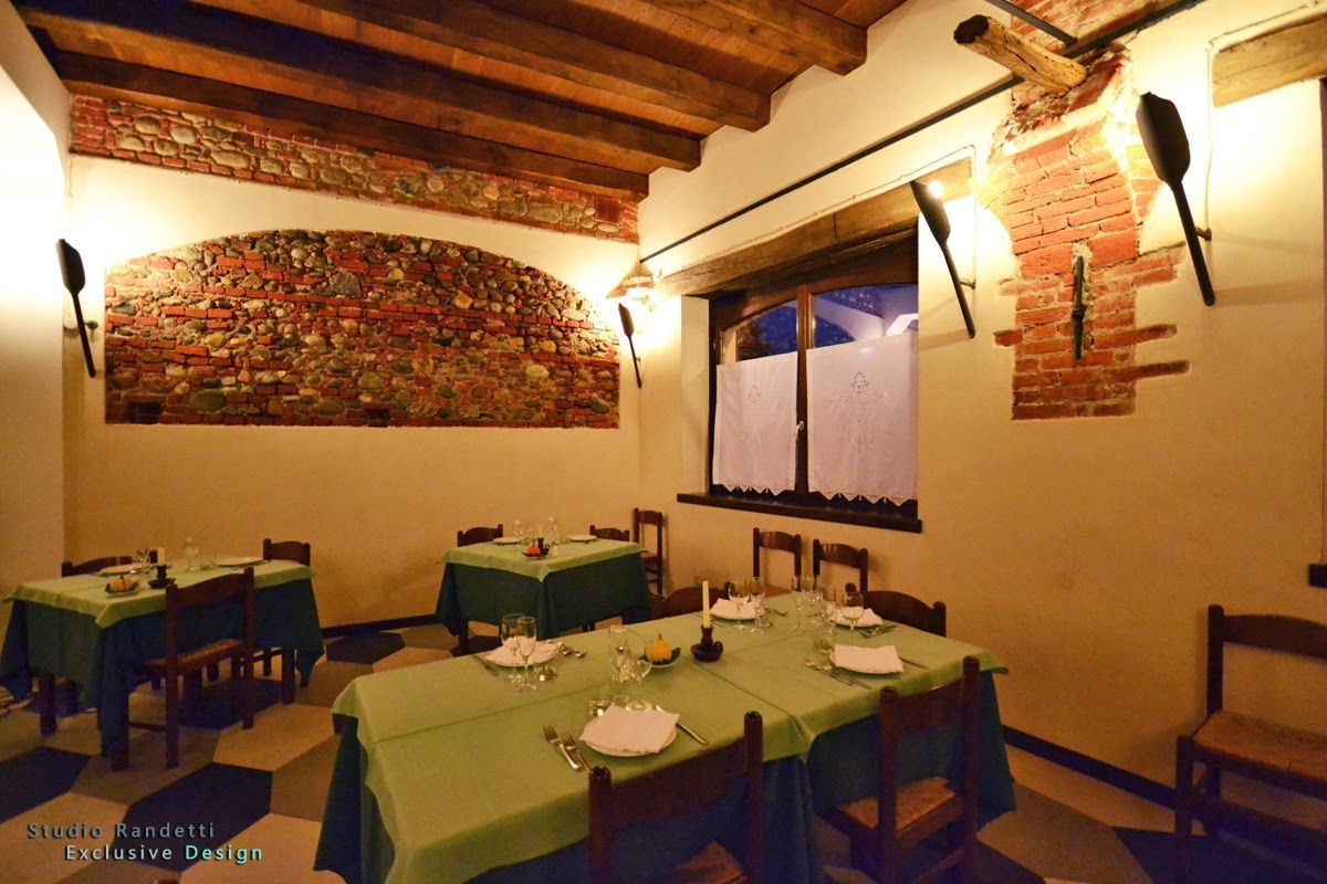 Accogliente sala da pranzo di un ristorante con tovaglie verdi, travi in legno a vista, opere d'arte alle pareti e luci calde.