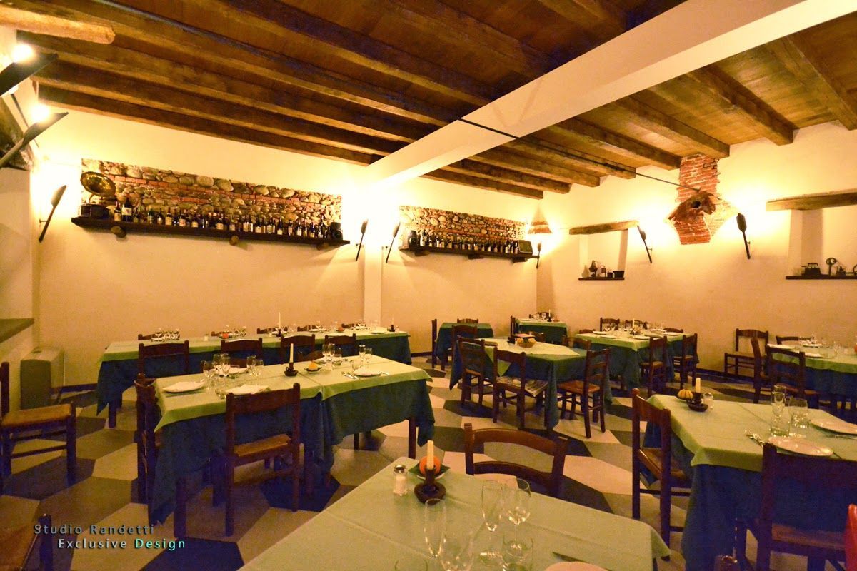 Sala da pranzo rustica e caldamente illuminata, con travi in legno a vista, tovaglie bianche e tavoli e sedie disposti con cura.
