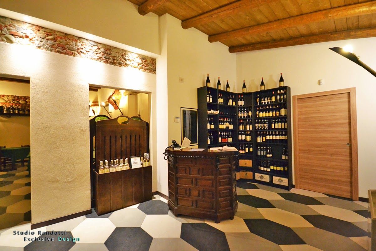 Interno di un'enoteca illuminato da una luce calda, con scaffali di bottiglie, banconi in legno e pavimento a scacchi.