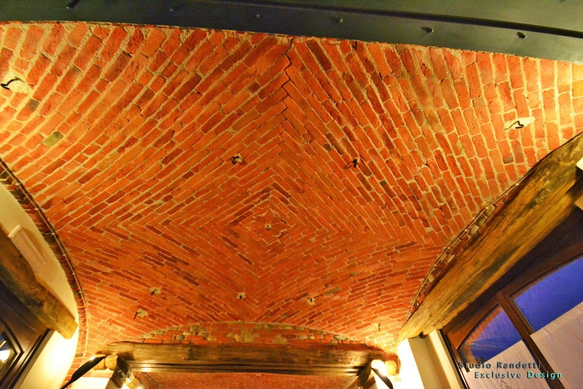 Soffitto a volta in mattoni con illuminazione calda e finestre con cornici blu lungo i lati.
